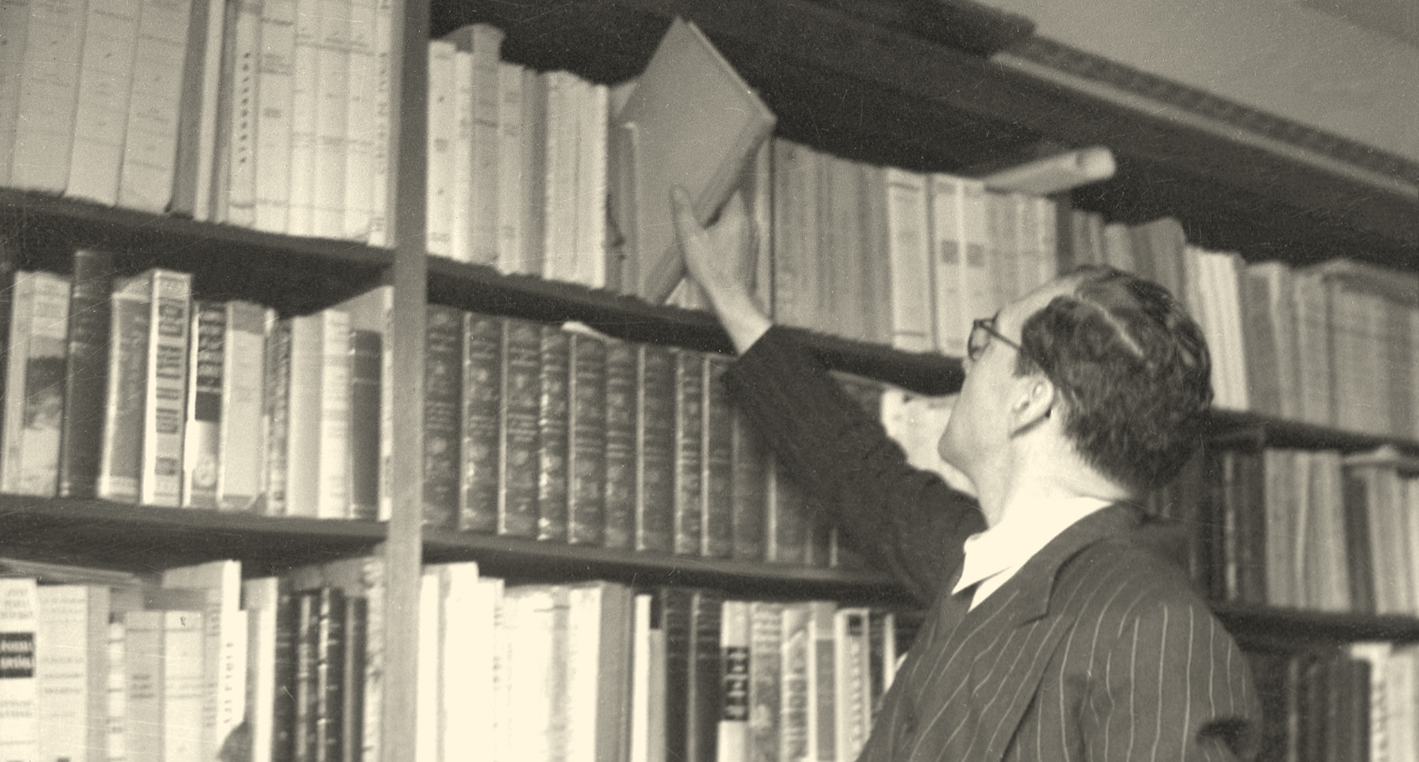 Foto antigua de un hombre una en biblioteca sacando un libro