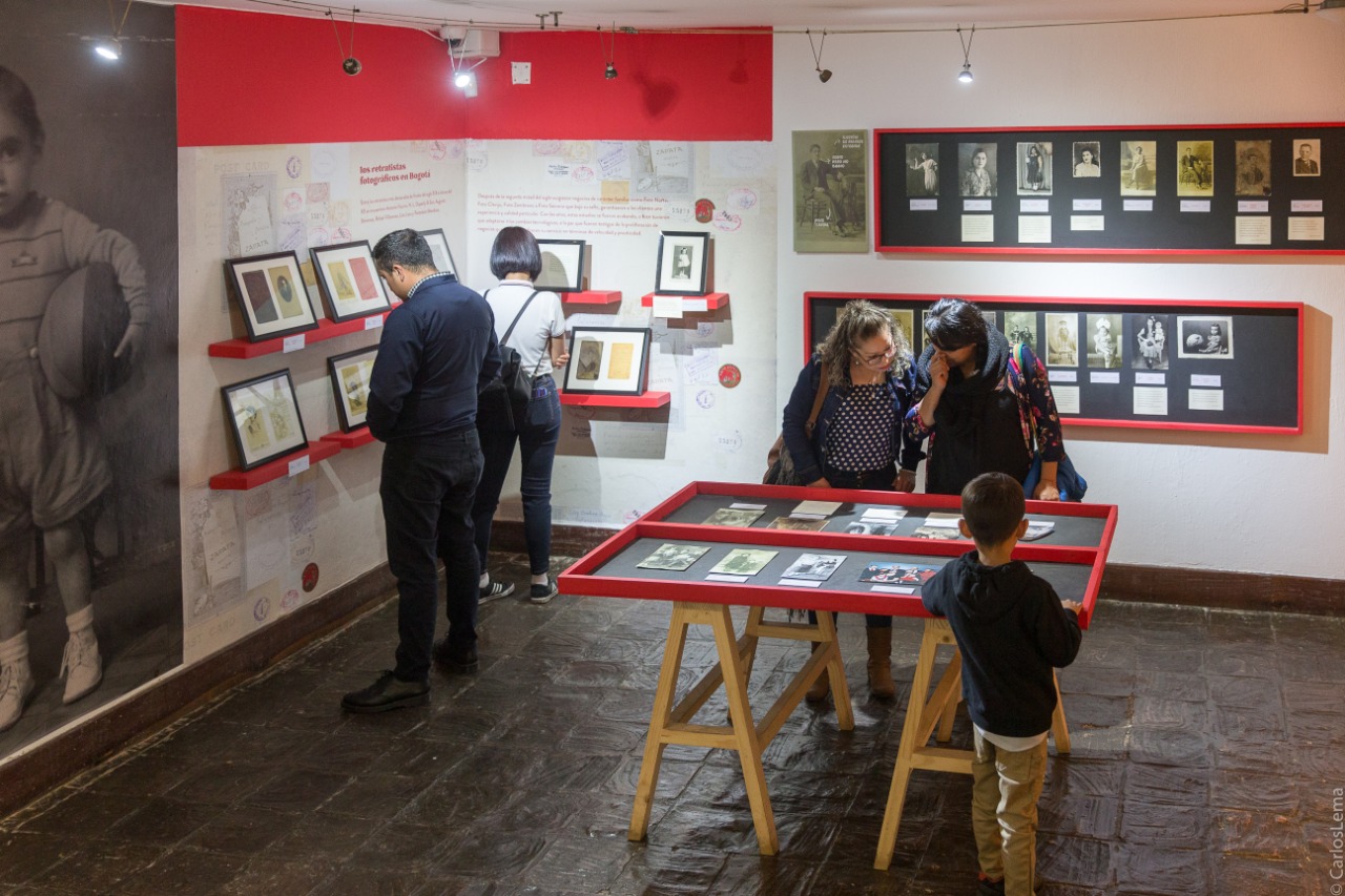 Cuatro personas y un niño observando los cuadros fotográficos en la exposición Temporal Álbum Familiar en la sede Casa Sámano del Museo de Bogotá