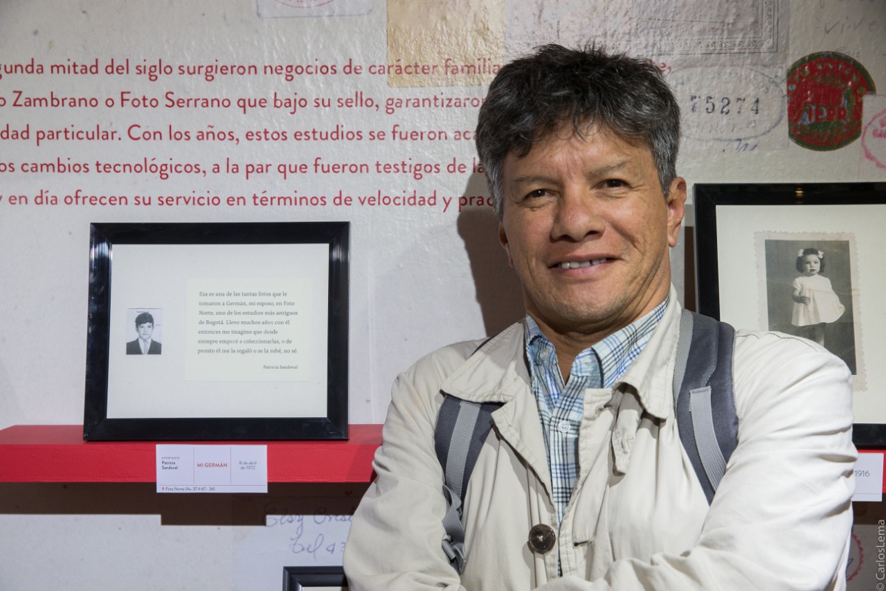 Fotografía de un hombre junto al cuadro de un exponente literario en la exposición Temporal Álbum Familiar en la sede Casa Sámano del Museo de Bogotá