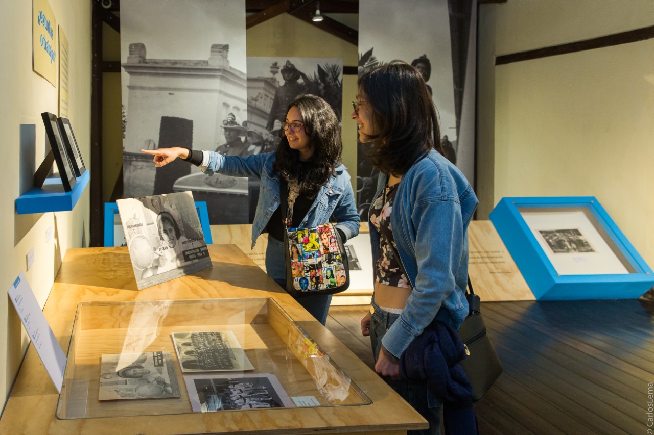 Dos mujeres sonriendo al observar los cuadros fotográficos en la exposición Temporal Álbum Familiar en la sede Casa Sámano del Museo de Bogotá