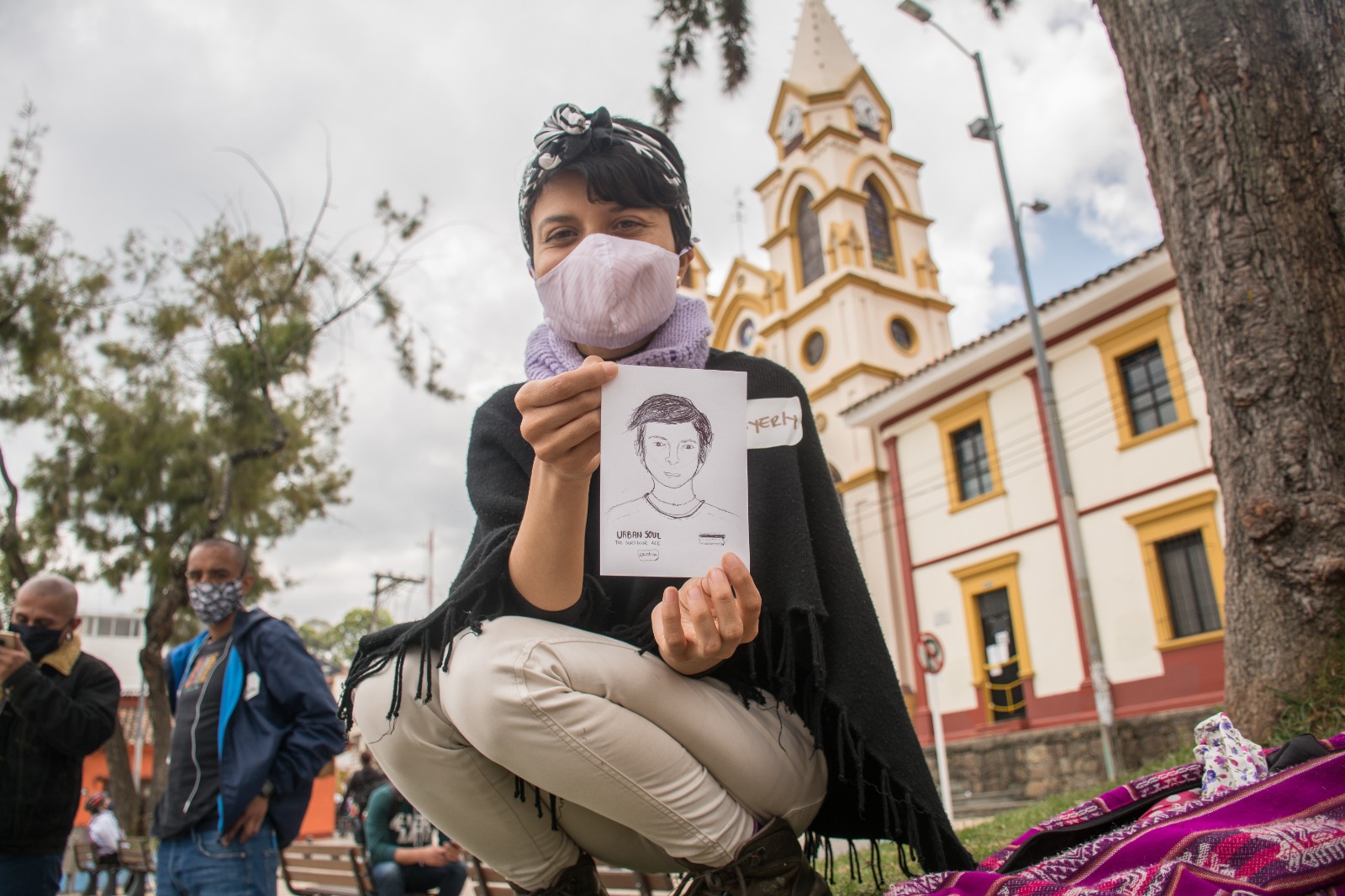Mujer frente a iglesia de Suba sosteniendo un dibujo de un hombre