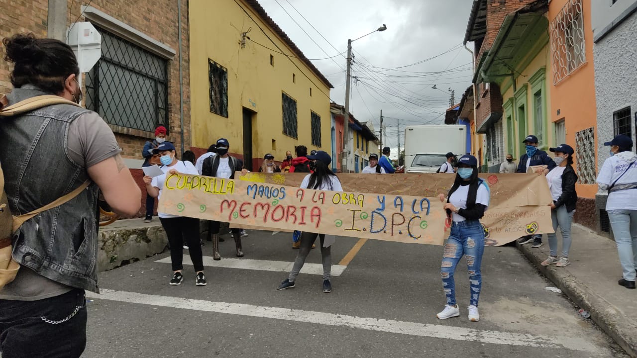 Grupo de personas caminando en la calle con una cartelera que dice Cuadrilla manos a la obra y la memoria IDPC