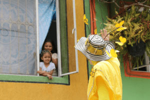 Persona con sombrero con mariposas saluda a niñas en una ventana