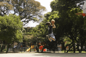Basquetbolista jugando en la cancha del Parque Brasil, espacio rodeado de árboles y juegos infantiles