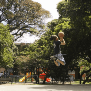 Basquetbolista jugando en la cancha del Parque Brasil, espacio rodeado de árboles y juegos infantiles