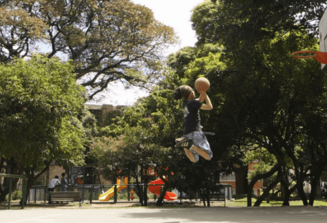 Basquetbolista jugando en la cancha del Parque Brasil, espacio rodeado de árboles y juegos infantiles