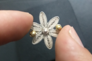 Dedos sosteniendo flor de plata realizada en filigrana