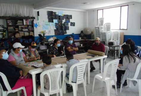 Personas en un salón de clase alrededor de una tira de papel kraft aportando a la construcción de la línea de tiempo del desarrollo del Barrio El Regalo.