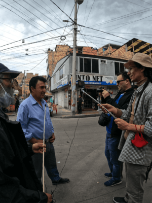 Tres personas entrevistan con cámaras y micrófonos a un hombre en medio de la calle de un barrio urbano.
