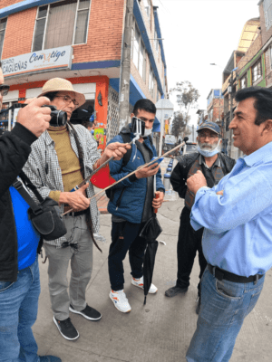 Cuatro personas entrevistan con cámaras y micrófonos a un hombre en medio de la calle de un barrio urbano.
