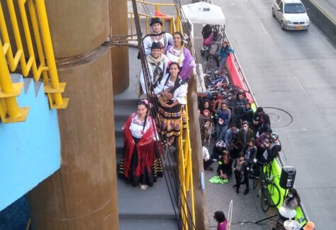 Grupo de danza con trajes típicos reunido para una foto realizada en las escaleras de un puente peatonal.