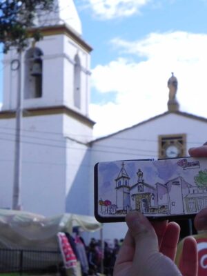 Manos exhiben dibujo de una iglesia enfrente de la verdadera iglesia dibujada a modo de comparación.