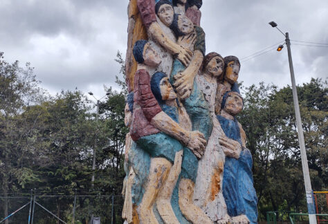 Escultura en un parque de varias personas juntas abrazadas y amontonadas en forma de columna.