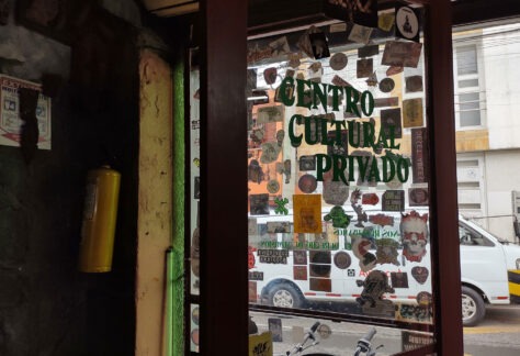 Puerta de vidrio de un establecimiento con varias calcomanías adheridas y con las palabras Centro Cultural Privado escrito en letras verdes