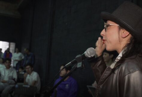 Mujer hablando con micrófono a los invitados al evento de proyección de las piezas audiovisuales en La Guarida del Zorro.