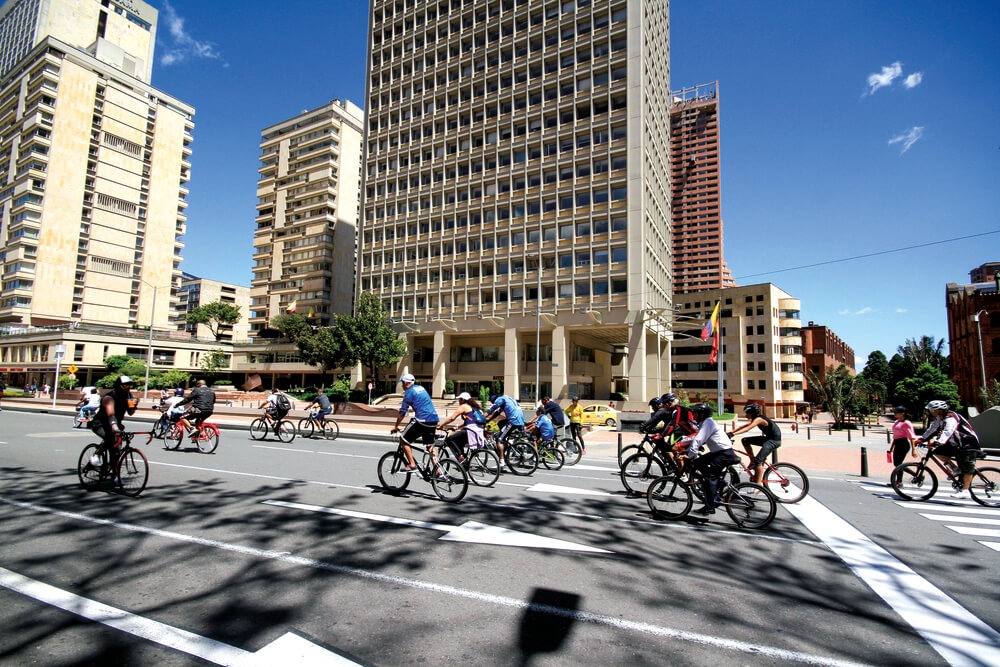 ciudadanos y ciudadanas montando bicicleta en un día soleado en Bogotá.