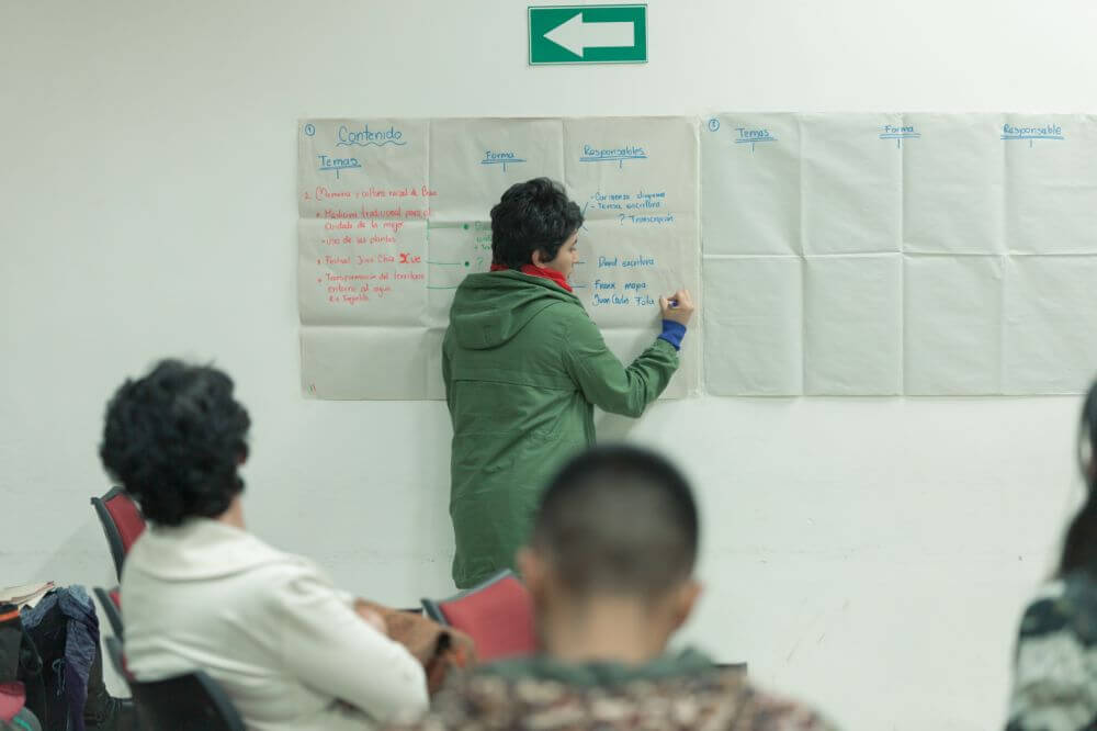 Mujer anotando ideas en una cartelera en el marco de un taller de investigación