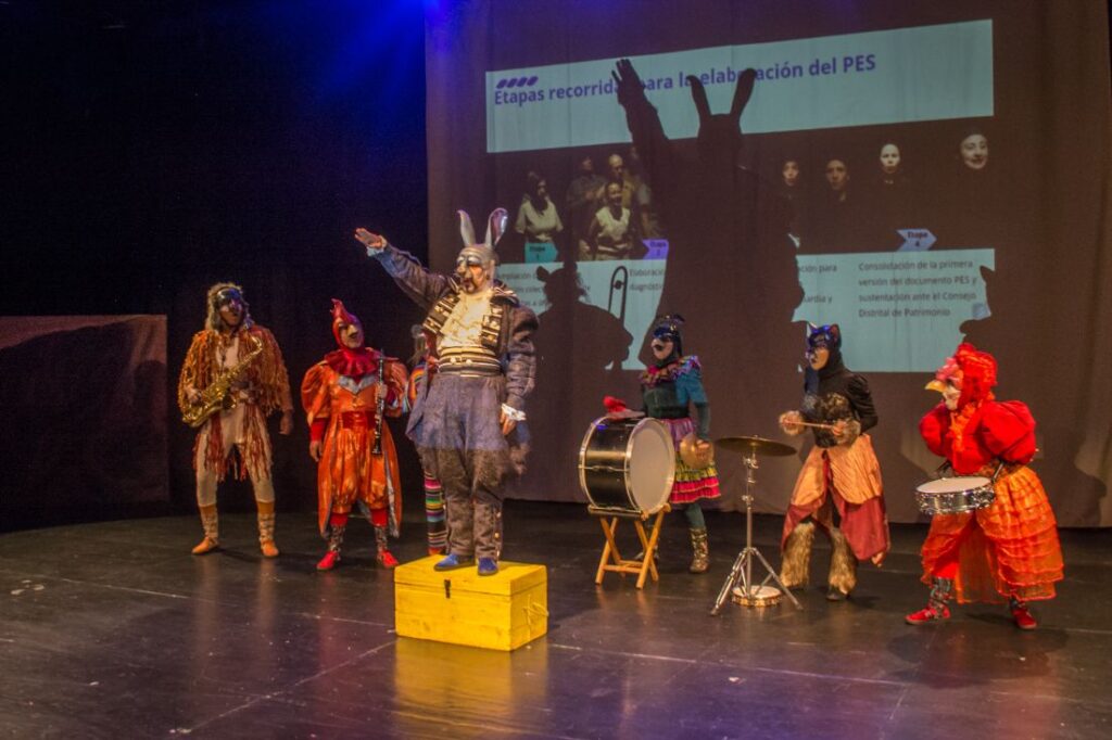 Un grupo de personas en el escenario con un hombre disfrazado durante la presentación de la Declaratoria de usos y la proyección artística y social del teatro de creación colectiva en Bogotá