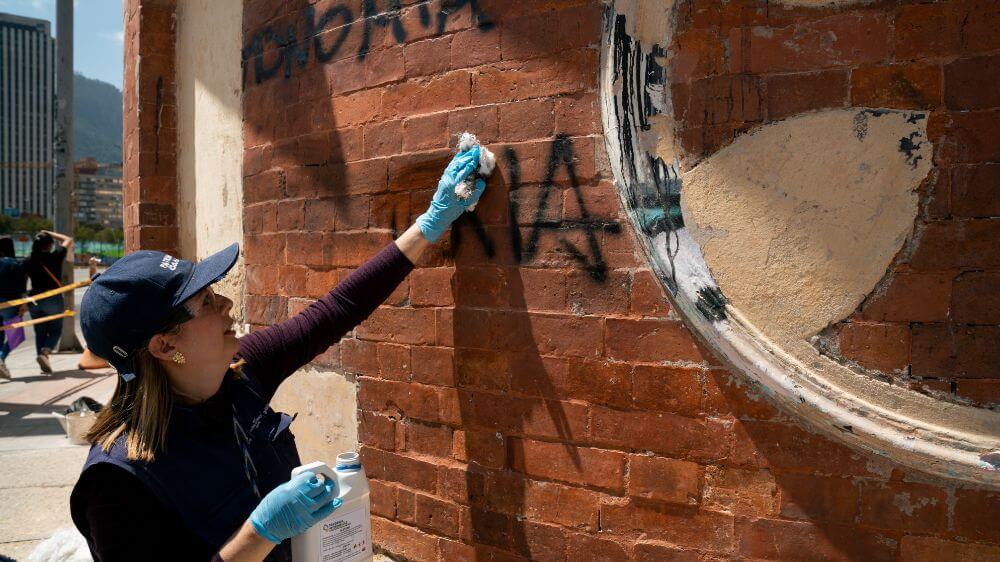 Mujer eliminando un graffitti la fachada del cementerio central.