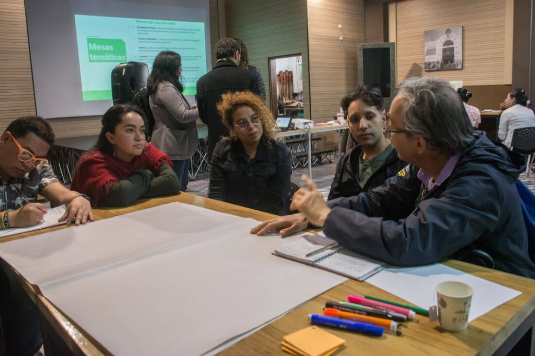 Grupo de personas sentadas alrededor de una mesa conversando del plan de desarrollo distrital