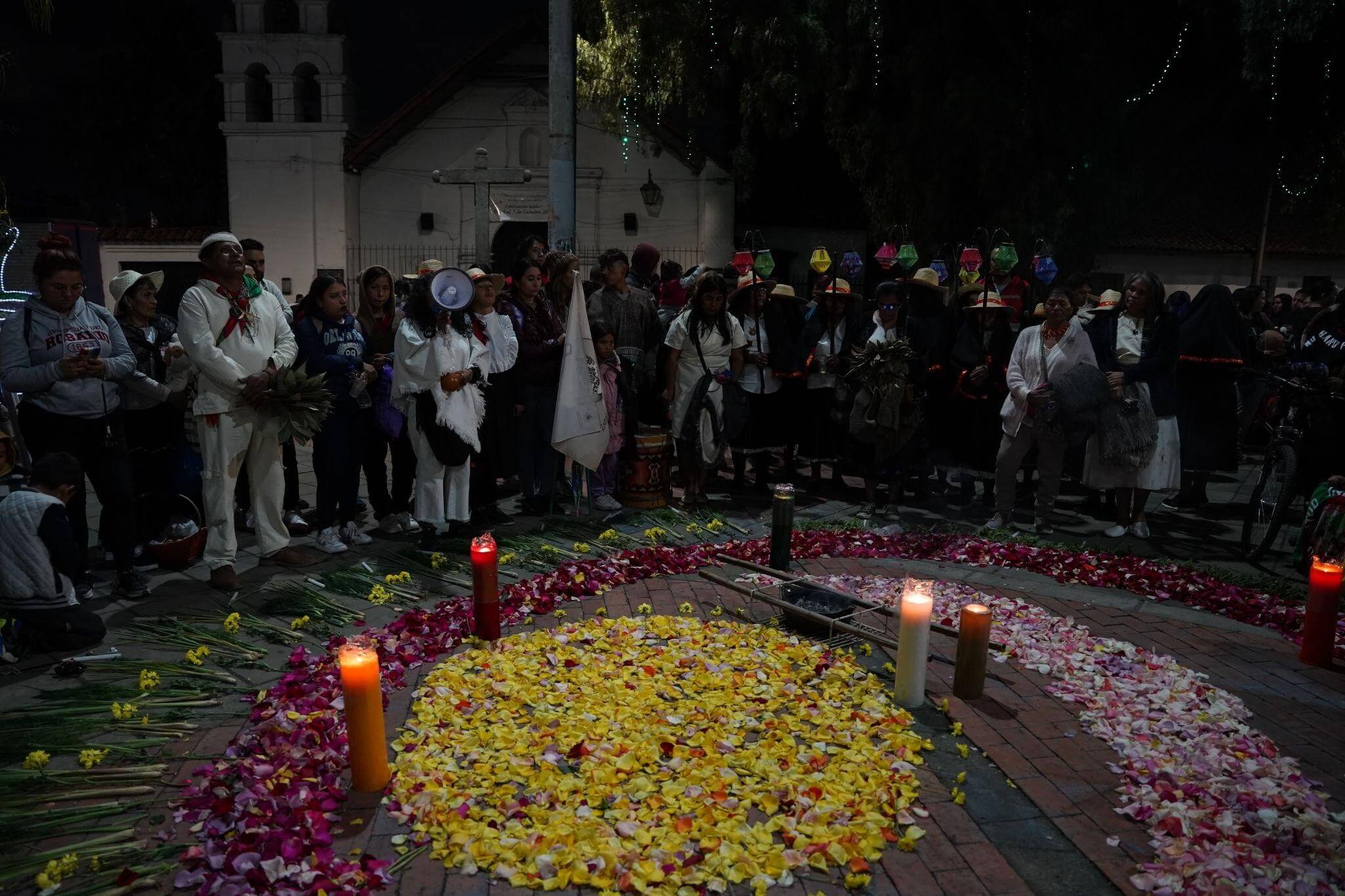 Personas se reúnen alrededor de un círculo de flores y velas durante el festival Jizca Chia Zhue.