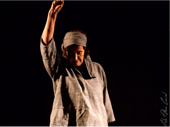 Patricia Ariza en el escenario con un vestido gris levanta la mano en el Teatro.