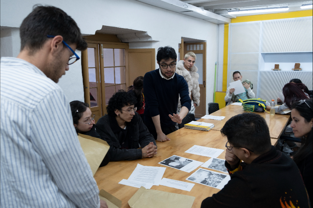 Grupo de personas al rededor de una mesa con fotrografías en blanco y negro