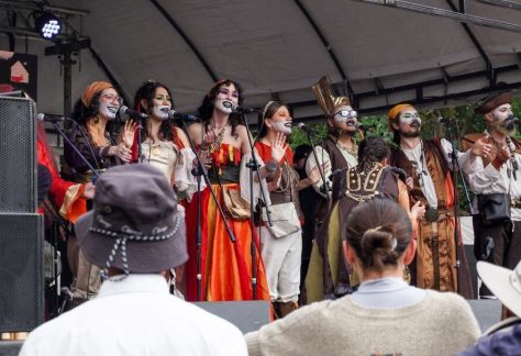 Grupo de actores y actrices con maquillaje teatral y vestuario de época canta en el escenario durante la Fiesta de Reyes Magos y Epifanía del barrio Egipto en Bogotá, ante un público reunido al aire libre.