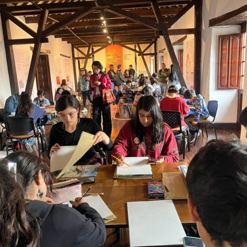 Vista general de una sala con mesas donde niños, niñas y adolescentes participan en el Premio Dibujatón