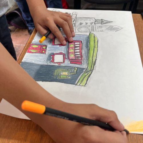 Niño colorea una ilustración de edificaciones durante el Premio Dibujatón para niños, niñas y adolescentes.