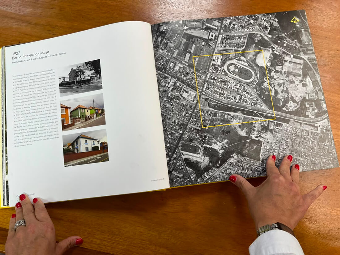 Vista en plano cenital de un usuario hojeando una publicación impresa desplegable con fotos e ilustraciones sobre una mesa de lectura.