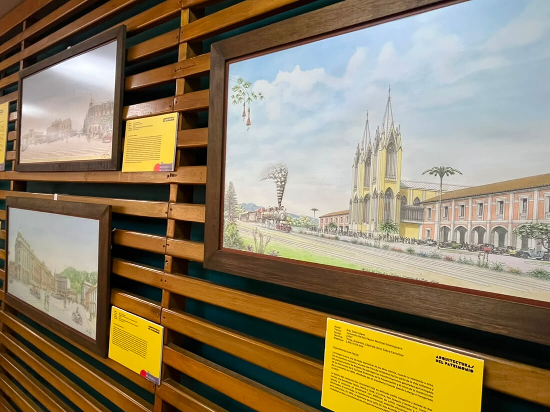 Panel de madera de la exposición «Arquitecturas Patrimoniales» con varias ilustraciones y grabados enmarcados de edificaciones históricas.