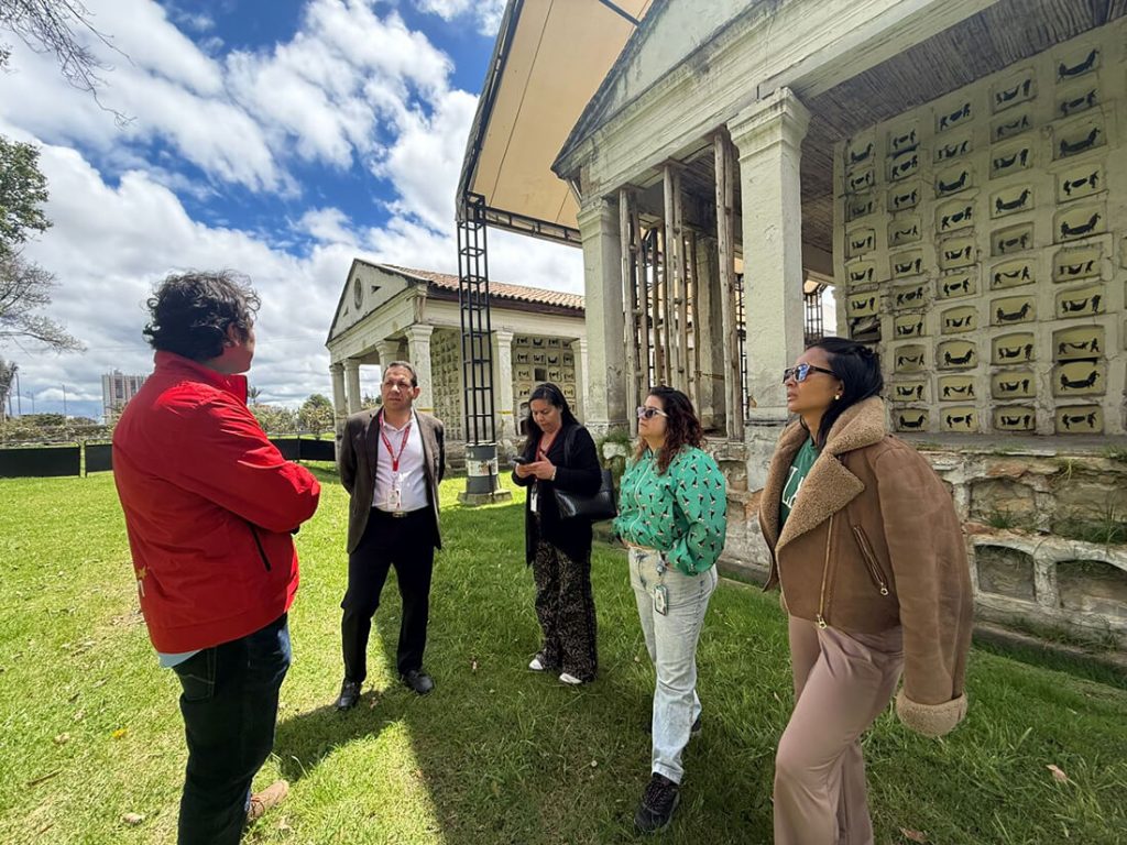 Estructura exterior de Los Columbarios en el Cementerio de Pobres de Bogotá, con la obra artística "Auras Anónimas" en sus nichos y un grupo de personas realizando un recorrido de memoria histórica.