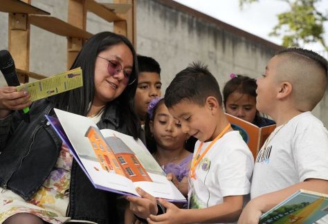 Una tallerista de Civinautas sonríe mientras le lee una cartilla a un grupo de niños sentados frente a ella, quienes escuchan con atención durante la jornada.