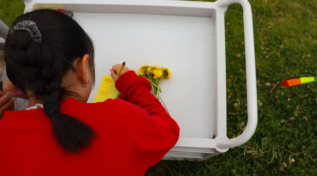 Niña escribe una nota junto a unas flores
