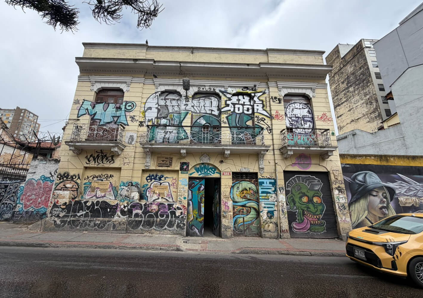 Fachada deteriorada de una casona colonial de dos pisos en la Calle 18 # 5 - 93, con grafitis, pintura desgastada en tono amarillo y deterioro visible en puertas y balcones de madera.