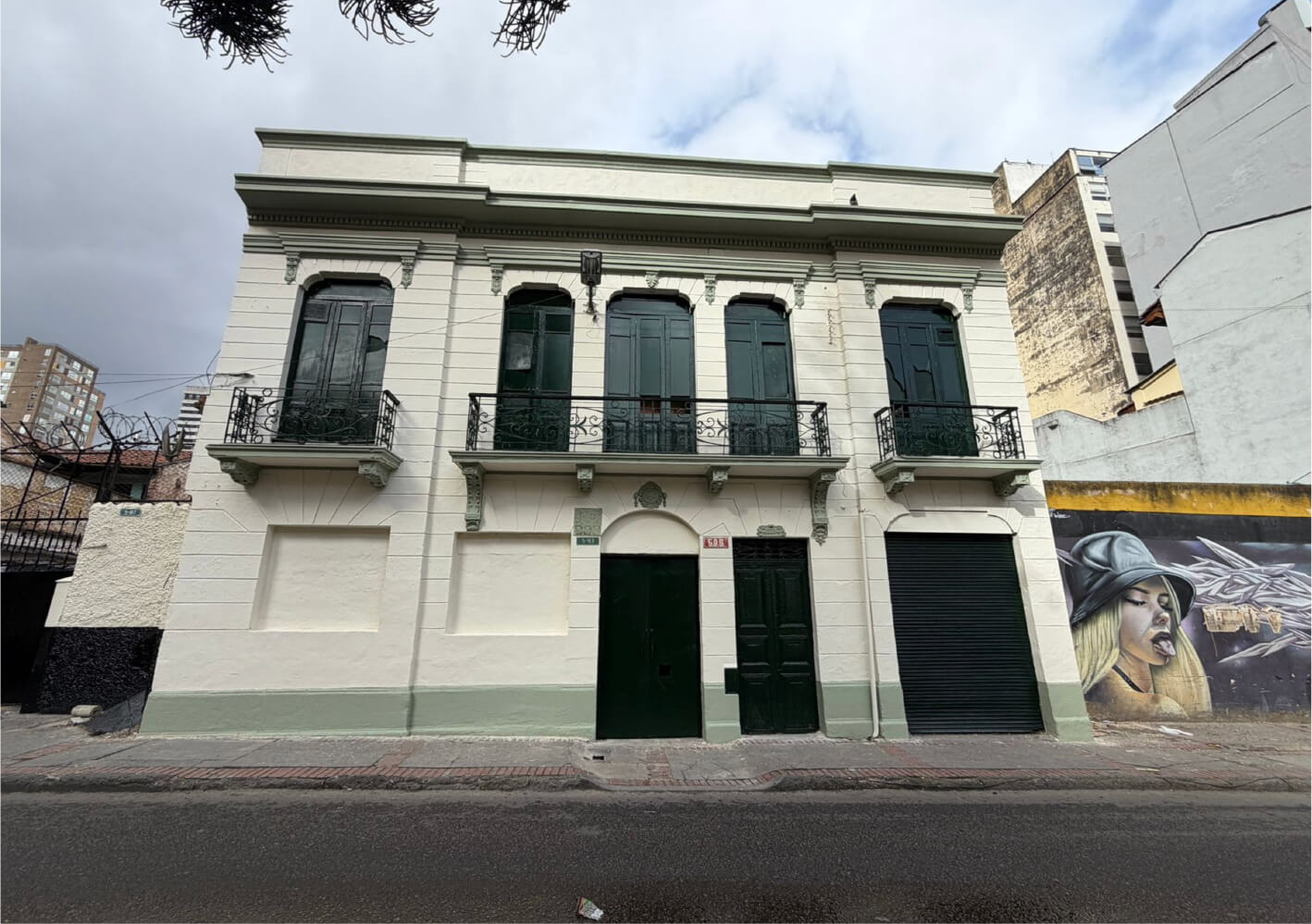 Fachada restaurada de la casona colonial en la Calle 18 # 5 - 93, con muros limpios en tono beige, marcos y balcones de madera pintados en verde oscuro y conservación de su arquitectura patrimonial.