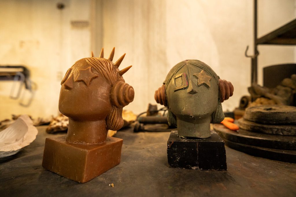 Dos bocetos tridimensionales o modelos de prueba en tono marrón dorado de la escultura "La Rockera", ubicados sobre una mesa de trabajo en el taller.