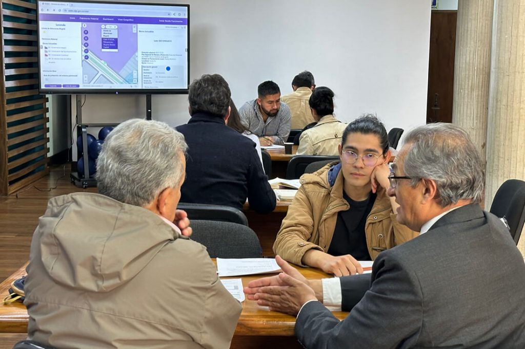 Dos ciudadanos conversan en un escritorio con un profesional del IDPC revisando documentos sobre una mesa durante la jornada de Aprobatón de Trámites.