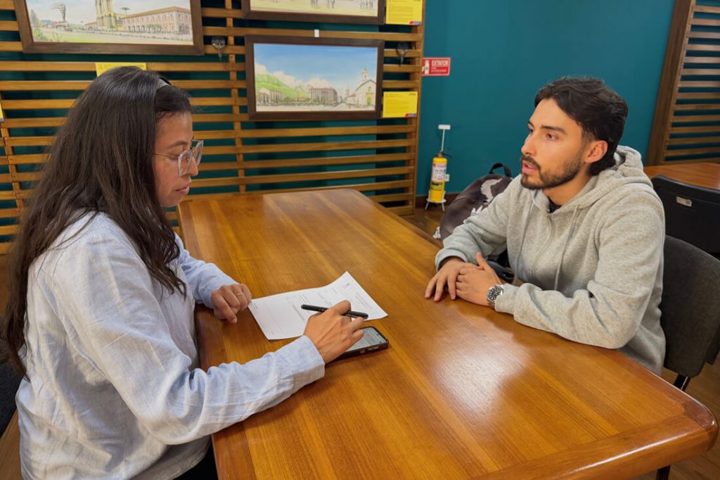 Ciudadano y profesional del IDPC reunidos en mesa de trabajo revisando documentos y planos.