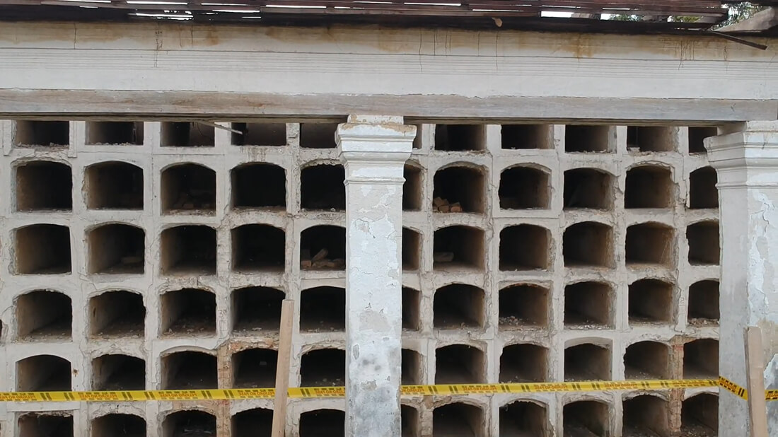 Vista frontal de las nichos en cuadrícula de la galería cementerial de Los Columbarios, acordonada con cinta de seguridad amarilla durante las labores de restauración.
