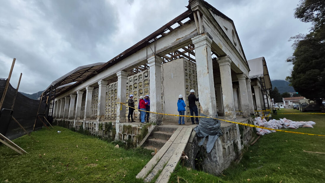 Perspectiva lateral de una de las estructuras de Los Columbarios rodeada por cintas de precaución y bolsas de material de obra, con operarios trabajando en sus alrededores.