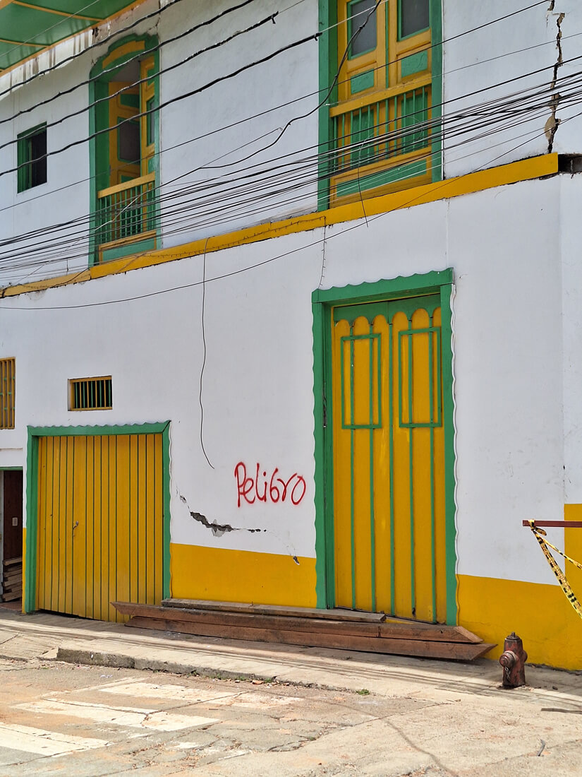 Fachada de una vivienda tradicional de arquitectura cafetera en El Cairo, con paredes amarillas y zócalos con la palabra «Peligro» pintada tras el sismo.