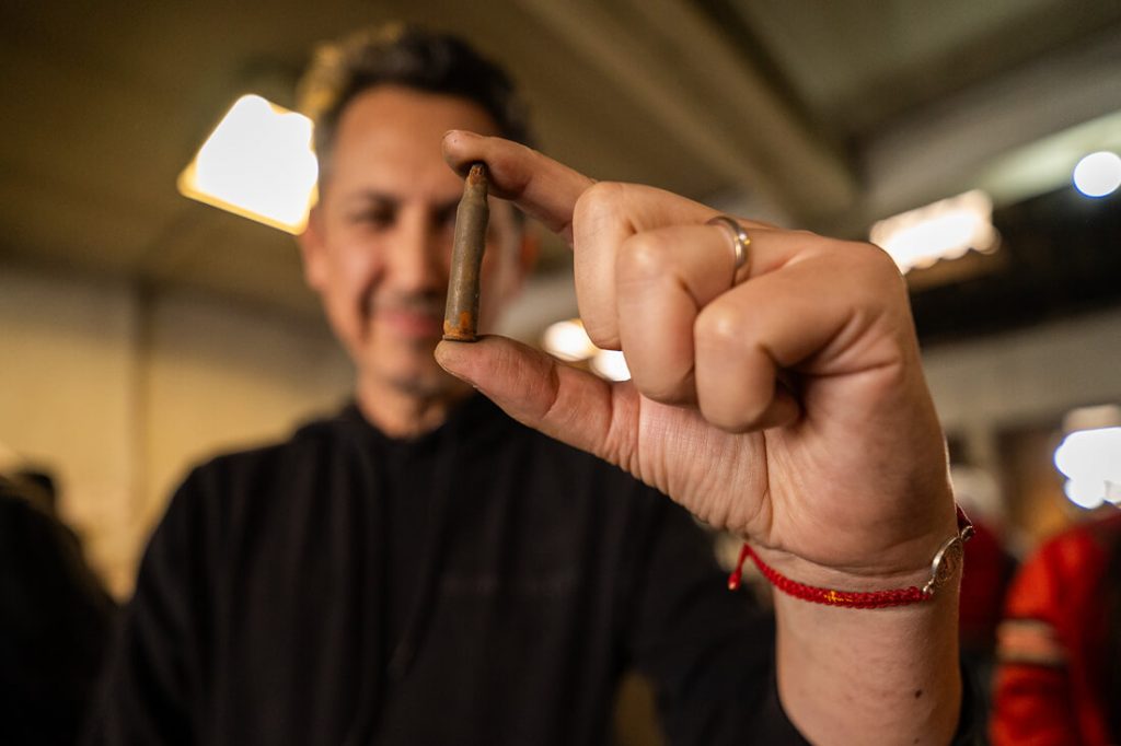 El artista bogotano Maquiamelo sonríe sosteniendo una bala metálica en su mano, una muestra del material reciclado utilizado para fundir la escultura "La Rockera" en el taller.