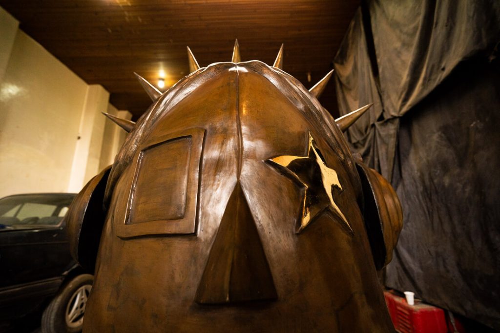 Primer plano en el taller de la cabeza en proceso de la escultura "La Rockera", destacando el detalle de la estrella sobre el ojo, los audífonos con taches y la superficie dorada del material.