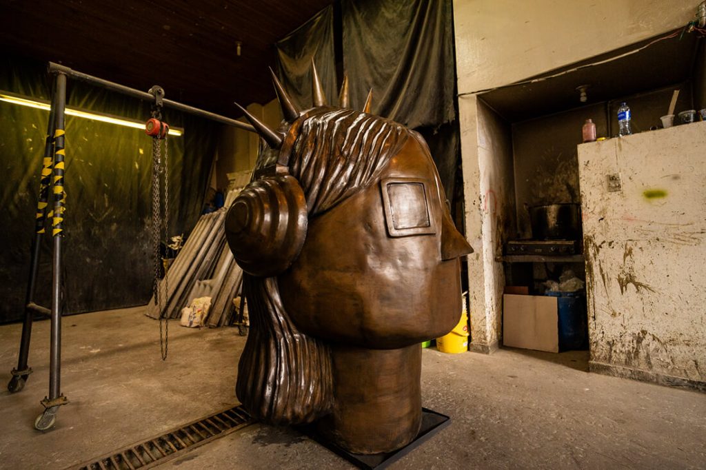 Vista lateral en el taller del proceso de modelado de la escultura "La Rockera" en tamaño real, mostrando los detalles de la cabeza, los audífonos y el perfil de la figura.