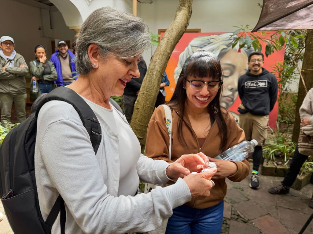 Dos participantes del recorrido patrimonial observan atentamente una pequeña pelota en la palma de la mano durante una actividad.
