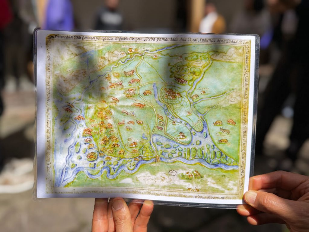 Manos sostienen una reproducción de un mapa antiguo de Bogotá durante el recorrido del IDPC.