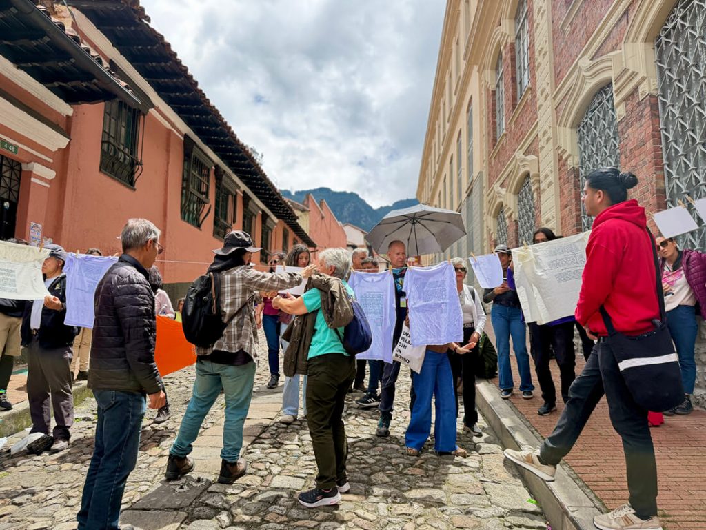 Asistentes al recorrido patrimonial del IDPC observan una tendida de ropa en la calle con camisetas que llevan impresas frases e imágenes históricas sobre el oficio de las lavanderas.
