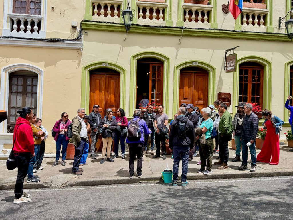 Grupo de asistentes y guías del recorrido patrimonial escuchando una explicación frente a la fachada colonial de una edificación histórica en Bogotá.